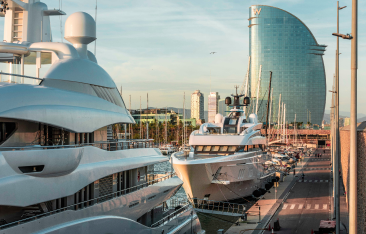 Marina with two superyachts in front of tall skyscraper.
