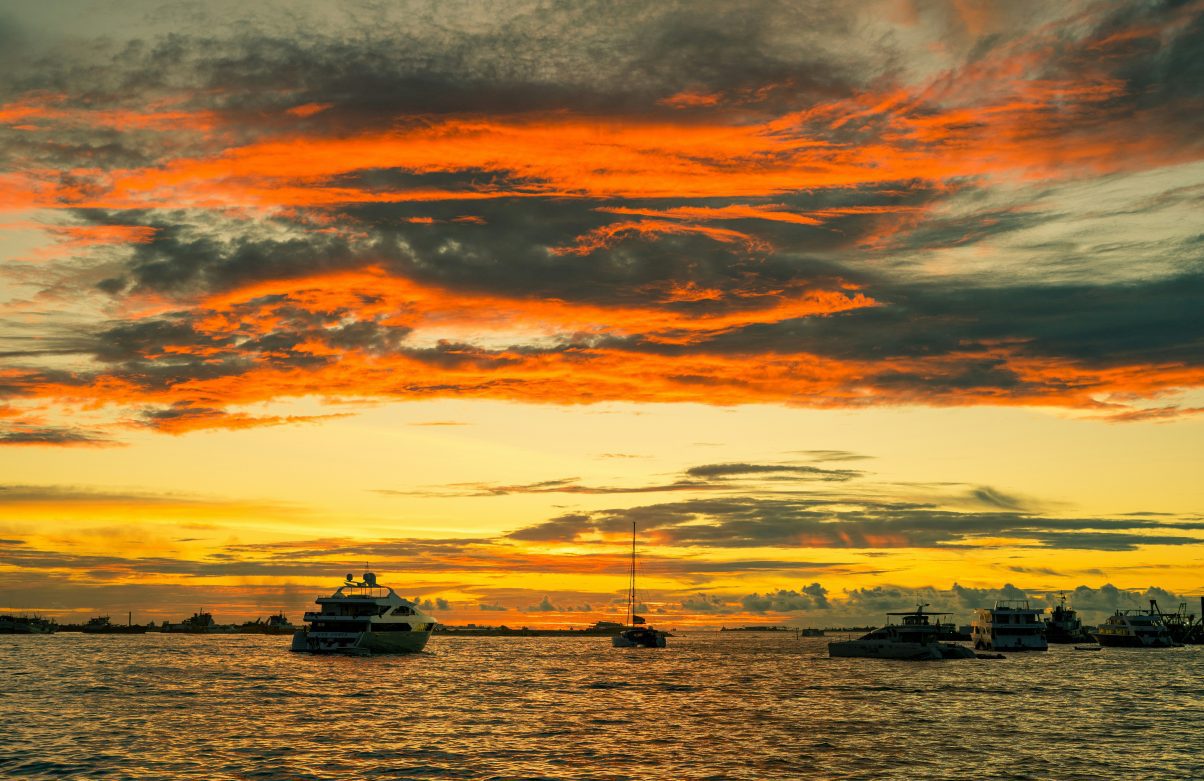 Superyachts on the sea at the Maldives under an orangey yellow sunset sky