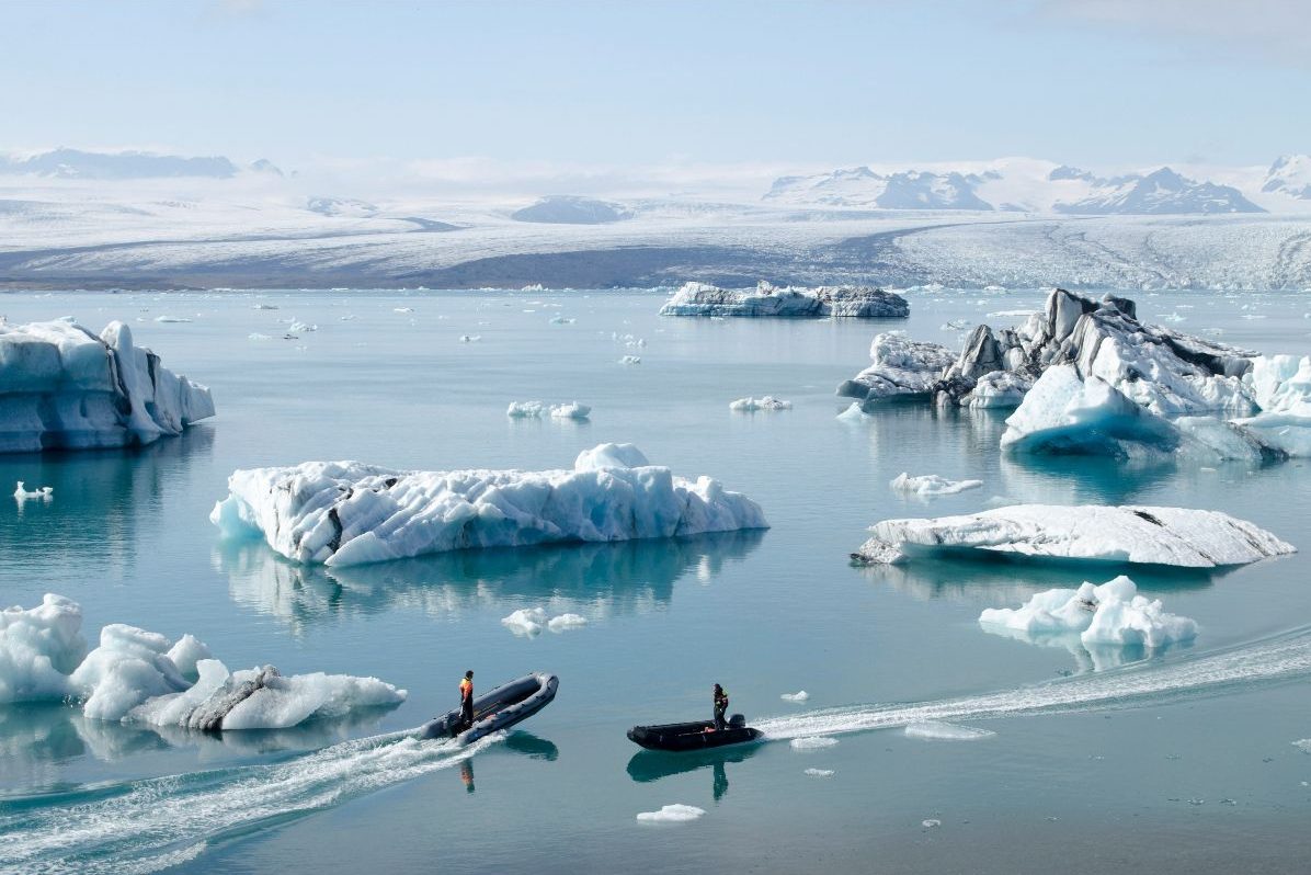 Iceland landscape of water and icebergs with two rib boats each with one person on. Land on the horizon